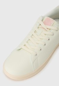 Sneaker in ecopelle verde chiaro con lacci piatti color crema, punta rotonda, dettagli laterali perforati e un discreto logo accentato sulla linguetta.