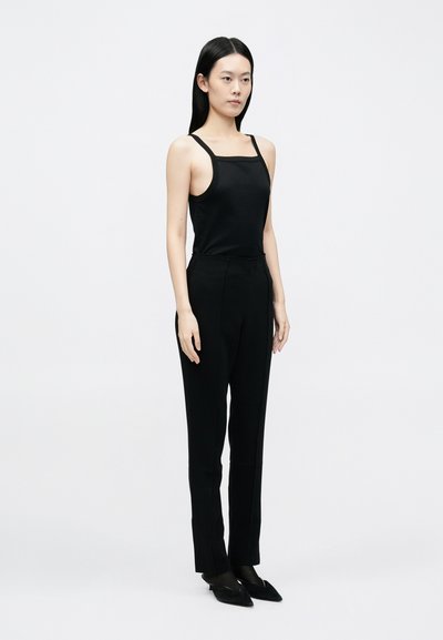 Fekete ujjatlan felső vékony pántokkal, hozzá illeszkedő fekete nadrággal és hegyes orrú fekete balerinacipővel. Egyszerű dizájn, sima anyag, letisztult sziluett.