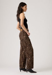 Hlače širokih nog z leopardjim vzorcem v rjavi in črni barvi, z visokim pasom in dvema sprednjima žepoma, kombinirane s črnim oprijetim topom in črnimi gležnjaki.