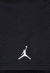 Fekete textúrájú szövet, amelyen cikkcakk minta található. A jobb alsó sarokban egy fehér Air Jordan logó helyezkedik el.