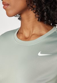 Hele roheline Nike särk, millel on sile tekstuur, ümmargune kaelus ja valge logo, mis on esile tõstetud vasakul küljel. Suumkaader kaelusest ja õlast.