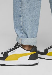 Černobílé tenisky s žlutým akcentem, s texturovaným svrškem, šněrováním a silnou bílou podrážkou. Neformální styl.