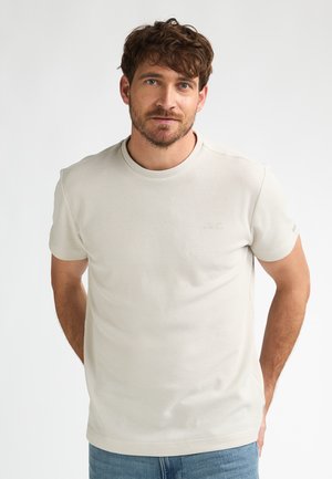 Lichtbeige T-shirt met korte mouwen, een gestructureerd ontwerp en een ronde halslijn. Voorzien van een klein logo op de borst en effen randen.