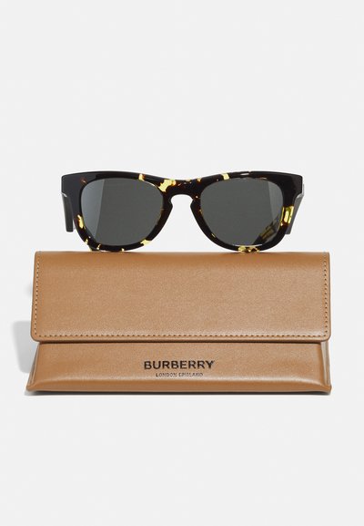 Ochelari de soare cu rame din scoică de broască țestoasă, cu lentile întunecate, așezați deasupra unei huse din piele maro, având un logo „Burberry” embosat și închidere tip snap.