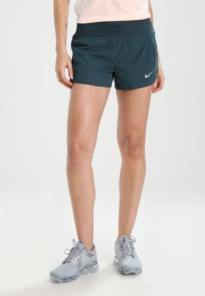 Shorts de sport teal avec une large ceinture et des poches latérales. Associés à des chaussures de course grises claires avec une tige en mesh et une semelle rembourrée.