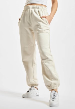 Cremefarvede joggerbukser med elastisk talje, sidelommer og ribbede manchetter med et diskret, mønstret design. Båret med hvide sneakers.