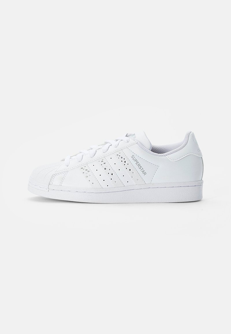 White leather sneaker with perforated three-stripe design and rubber sole. Features a textured toe cap and logo detail on the side.
