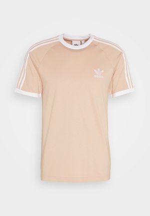 Beige Baumwoll-T-Shirt mit weißen Raglanärmeln und Saum. Auf der linken Brust befindet sich ein gesticktes weißes Adidas-Logo und auf den Ärmeln sind drei Streifen.