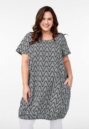 Luftiges Kleid mit Zickzackmuster in Schwarz und Weiß, kurzen Ärmeln, rundem Ausschnitt und seitlichen Taschen. Sanfte Stofftextur.