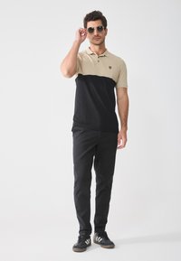 Kortermet polo-skjorte i beige og svart fargeblokkdesign, laget av bomull. Godt kombinert med svarte bukser og svarte joggesko.