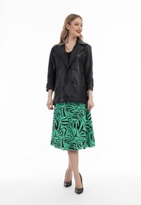 Schwarze Leder-Doppeltbindermantel mit spitzem Kragen, kombiniert mit einem knielangen grünen Rock mit einem schwarzen Zebra-Print.