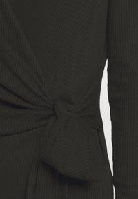 Gros plan sur un tissu côtelé noir avec un détail de nœud à la taille sur un vêtement à manches longues.