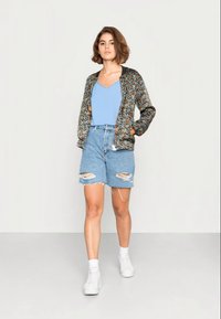 Jacket bomber preta com padrão floral, top azul claro em forma de V, calções de ganga rasgados e sapatilhas brancas. Textura suave, design casual.