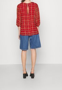 Top de cuadros rojos con mangas abullonadas y un escote en forma de ojo de cerradura, combinado con pantalones cortos de mezclilla y zapatillas negras de tacón bloque.