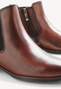 Stivaletti in pelle marrone con finitura liscia, zip laterale e pannelli elasticizzati. Design elegante con punta arrotondata e tacco basso.