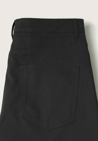 Pantalons en denim noirs avec une texture lisse, comportant une poche arrière, des détails de couture subtils et une boucle de ceinture en haut.