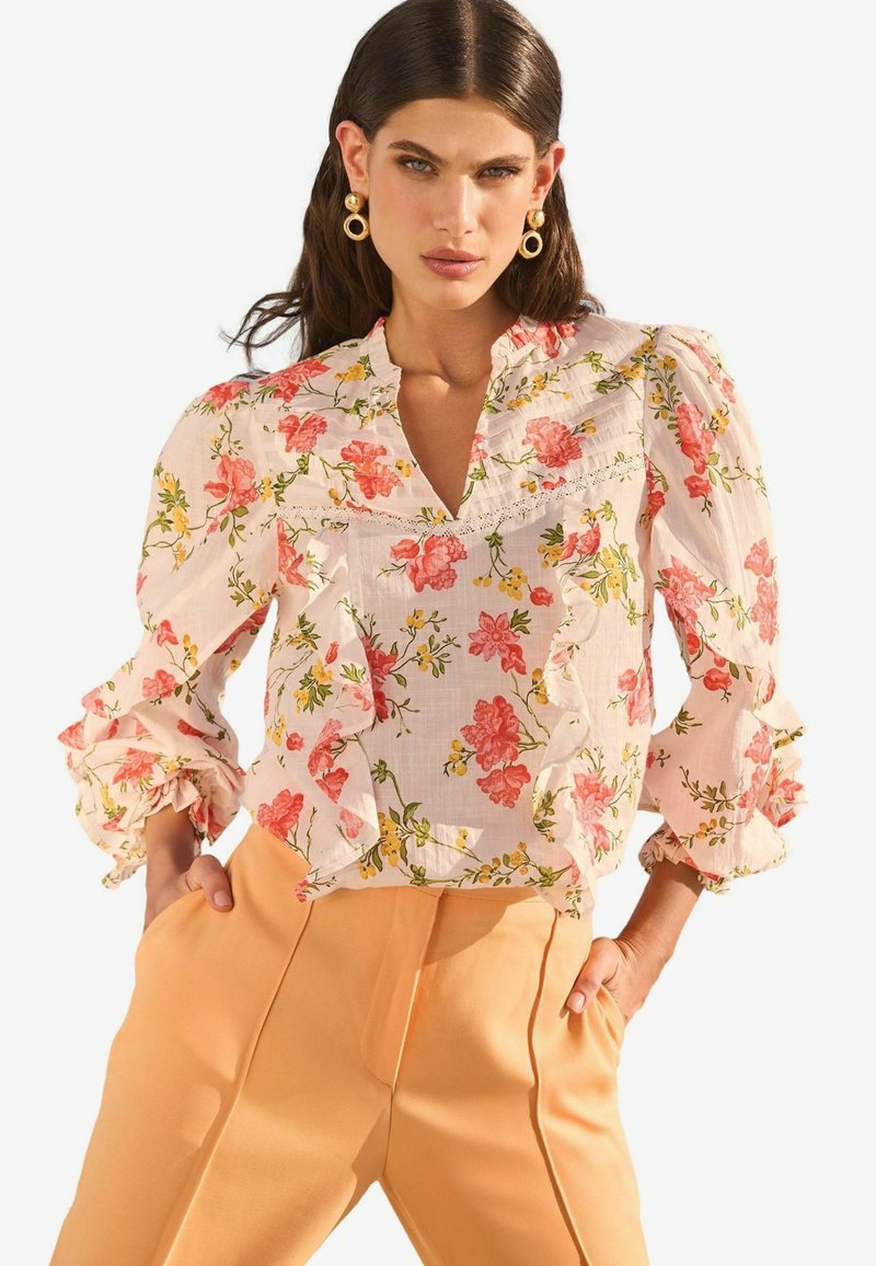 Blusa floreale con motivi rosa e gialli, maniche a volant e scollatura a V, abbinata a pantaloni pesca a vita alta.
