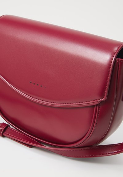 Borsa a tracolla in pelle bordeaux con superficie liscia, forma arrotondata, chiusura a soffietto e nome del marchio impresso. Inclusa tracolla regolabile.