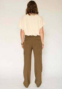 Haut beige à manches courtes associé à un pantalon cargo taille haute à jambes larges en vert olive, avec des poches latérales et une texture lisse.
