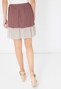 Mujer con una falda marrón con lunares y un dobladillo con volantes de rayas blancas, usando sandalias de tacón beige, vista desde atrás.