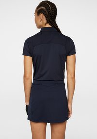 Polo shirt de sport bleu marine à manches courtes et dos texturé ; associé à une jupe assortie. Caractéristiques : coutures plates et silhouette épurée.