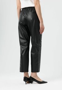 Zwarte nepleren broek met een ontspannen pasvorm, cropped lengte, elastische tailleband en twee achterzakken. Gecombineerd met zwarte puntige hakken.