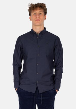 Navy-blaues Hemd mit Knöpfen aus einem glatten Stoff, mit Kragen, langen Ärmeln und schwarzen Akzenten, kombiniert mit samtigen navy-blauen Hosen.
