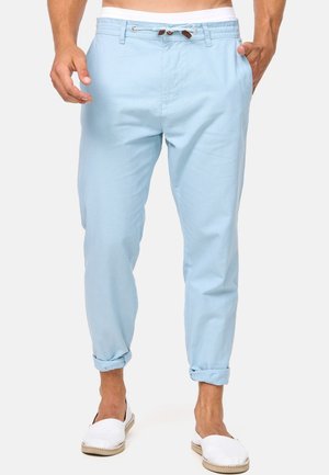 Pantalon décontracté bleu clair roulé avec taille à cordon porté par une personne debout portant des chaussures blanches sans lacets.