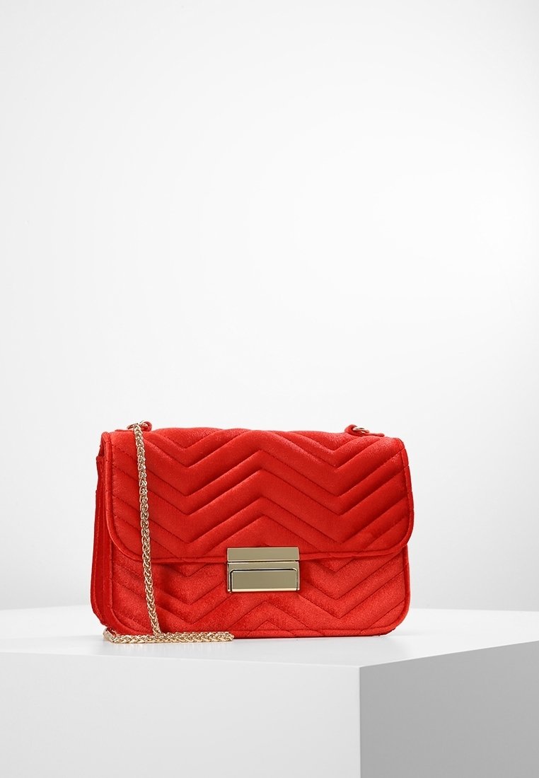 Červená prošívaná sametová kabelka přes rameno s chevronovým designem. Má zlatý klips a řetízkový popruh. Kompaktní s obdélníkovým tvarem.