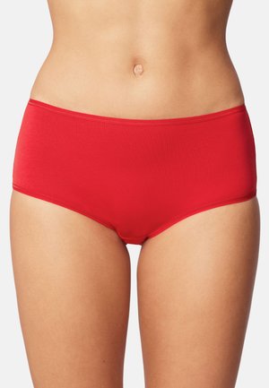 Sección media de una mujer vistiendo ropa interior hipster de algodón rojo liso sobre un fondo blanco.