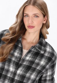 Fekete-fehér kockás gombos dzseki, galléros nyakkal, puha tapintással és elülső gombokkal. Stílusos kockás mintázat jellemzi.