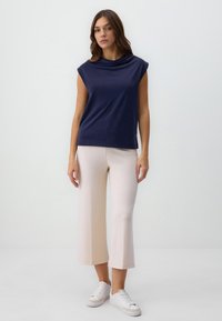 Top navy con collo a scaldacollo e maniche a cappuccio, abbinato a pantaloni a gamba larga beige chiaro e sneakers bianche. Tessuto liscio con design minimalista.