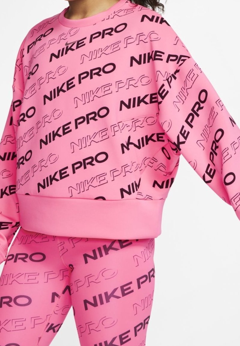 Felpa rosa con testo nero "NIKE PRO", vestibilità oversize, polsini a coste e leggings abbinati che presentano anch'essi il marchio "NIKE PRO" nei medesimi colori.