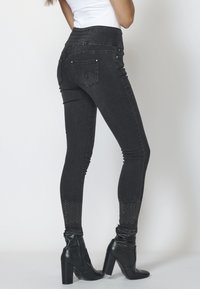 Svarta denim skinny jeans med hög midja, dekorerade med silverfärgade nitar vid anklarna och en smal silhuett.