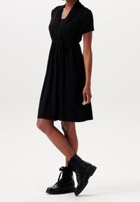Czarna sukienka z krótkimi rękawami, dekoltem w kształcie litery V, ściągniętą w talii i zwiewnym dołem, połączona z czarnymi butami wojskowymi. Gładki materiał i minimalistyczny design.