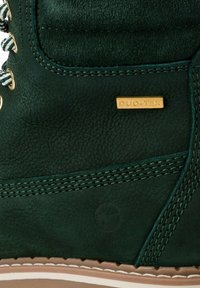 Grön läderstövel med guldhandtag, texturerad överdel, dubbel-lagerdesign och en ljusbrun gummisula med vita sömdekorationer.