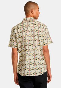 Short-sleeve shirt made of light fabric, featuring a repeating colorful pattern of stylized leaves on a beige background.
