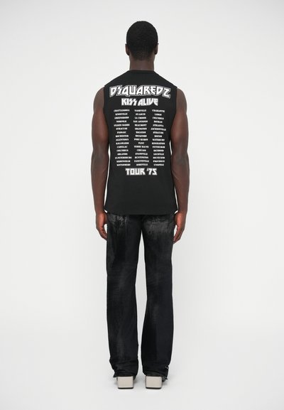 Sort ærmeløs trøje med hvid tekst med turnédatoer og steder på bagsiden. Kombineret med mørke udvidede jeans og lyse sko.