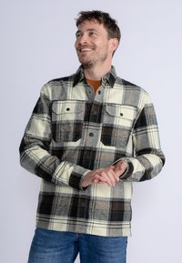 Károvaná flanelová košile v krémové, �černé a hnědé barvě. Obsahuje dvě náprsní kapsy, zapínání na knoflíky a uvolněný střih. Měkká textilie.