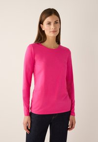 Long-sleeve T-shirt in vibrant pink, made from soft fabric with a round neckline and slim fit, paired with dark jeans.
