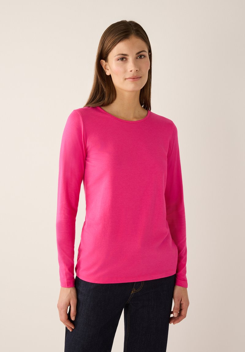 Long-sleeve T-shirt in vibrant pink, made from soft fabric with a round neckline and slim fit, paired with dark jeans.