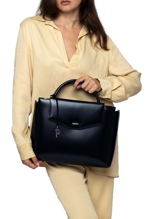 Zwarte leren handtas met gestructureerd ontwerp, ovale bovenhandvatten, voorflap en zilverkleurige details. Model draagt een lichtgele blouse.