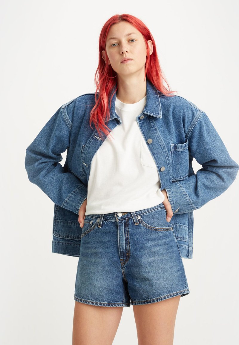 Giubbotto di jeans con una vestibilità ampia, lavaggio azzurro chiaro e due tasche frontali, abbinato a pantaloni corti di jeans a vita alta con un lavaggio coordinato.