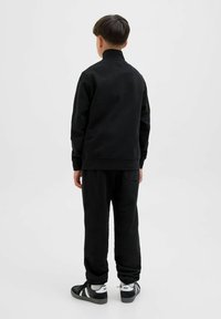 Svart sweatshirt med hög krage och ribbade ärmslut, tillsammans med matchande svarta sweatpants. Har en bakficka på byxorna.