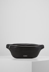 Borsa a vita in pelle nera texture con zip argento e logo "HUGO", esposta su un piedistallo bianco contro uno sfondo grigio.