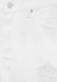 Gros plan sur un jean en denim blanc mettant en valeur la poche avant, la passants pour ceinture, le bouton en métal et un détail d’effilochage près de l'ourlet.