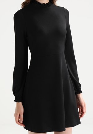 Czarna sukienka z długim rękawem, wysokim kołnierzem z falbanką i elastycznymi mankietami, posiadająca dopasowaną górę i rozkloszowany dół. Gładka faktura materiału.