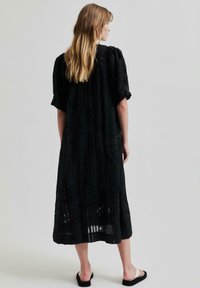 Robe noire en tissu texturé, coupe ample, longueur mi-mollet et manches courtes. Présente un motif subtil et un ourlet arrondi.
