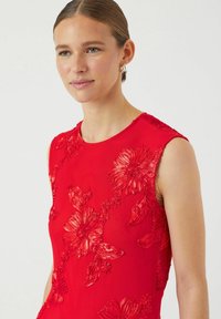 Rød ermeløs kjole med hevet blomstermønster i ulike nyanser av rødt. Glatt tekstur med en figursydd silhuett og rund hals.