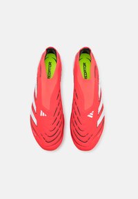 Chaussures de sport rouges avec une tige texturée, présentant des rayures blanches et une semelle intérieure vert fluo. Conception à enfiler avec une forme épurée.